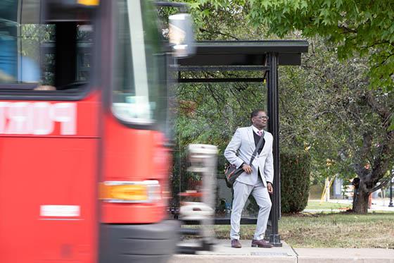 Photo of a man waiting for a bus, with a blurred bus passing into the frame