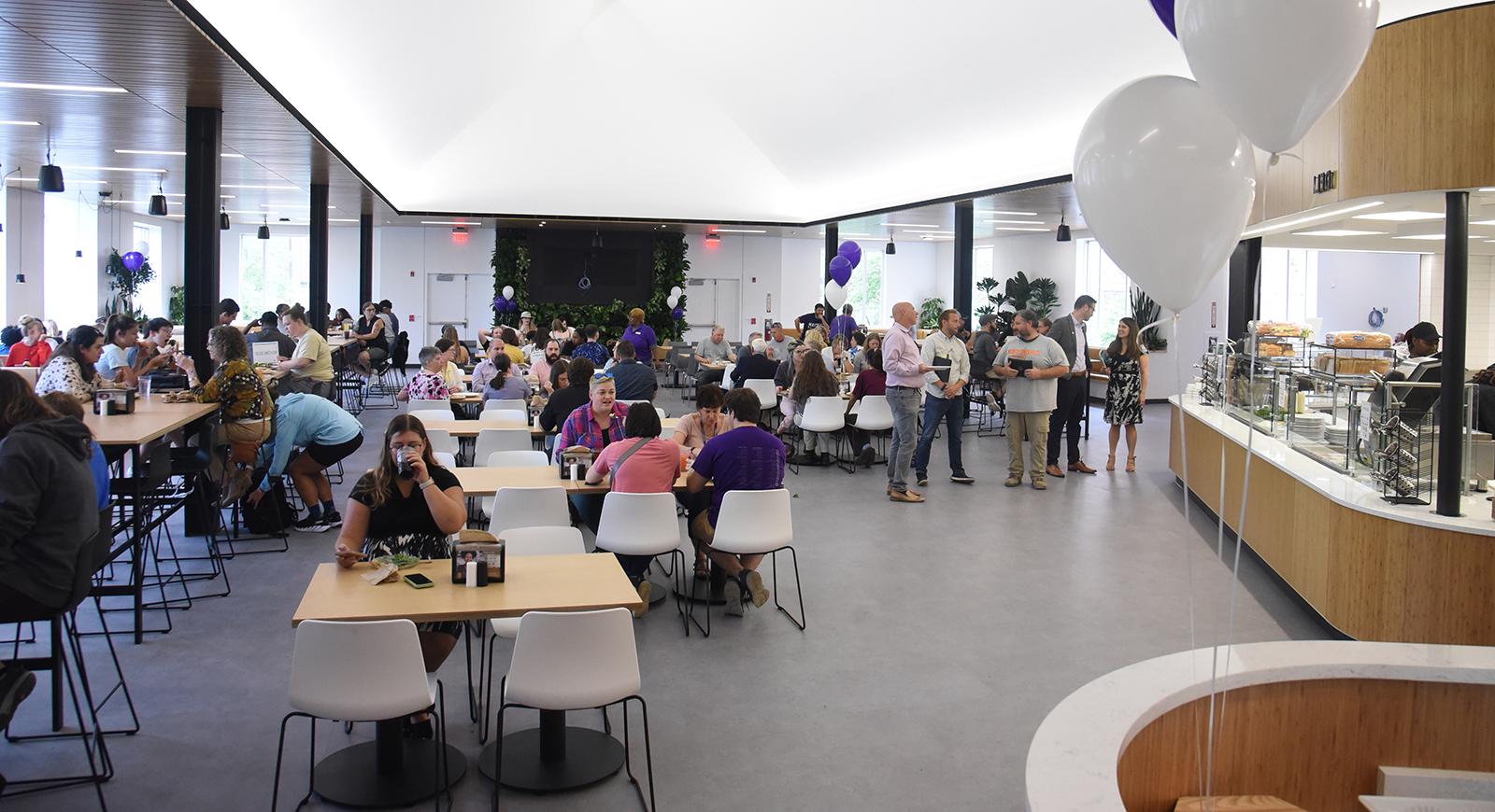 Photo of a crowded Anderson Dining Hall on opening day, with people eating and talking. There are many purple balloons.